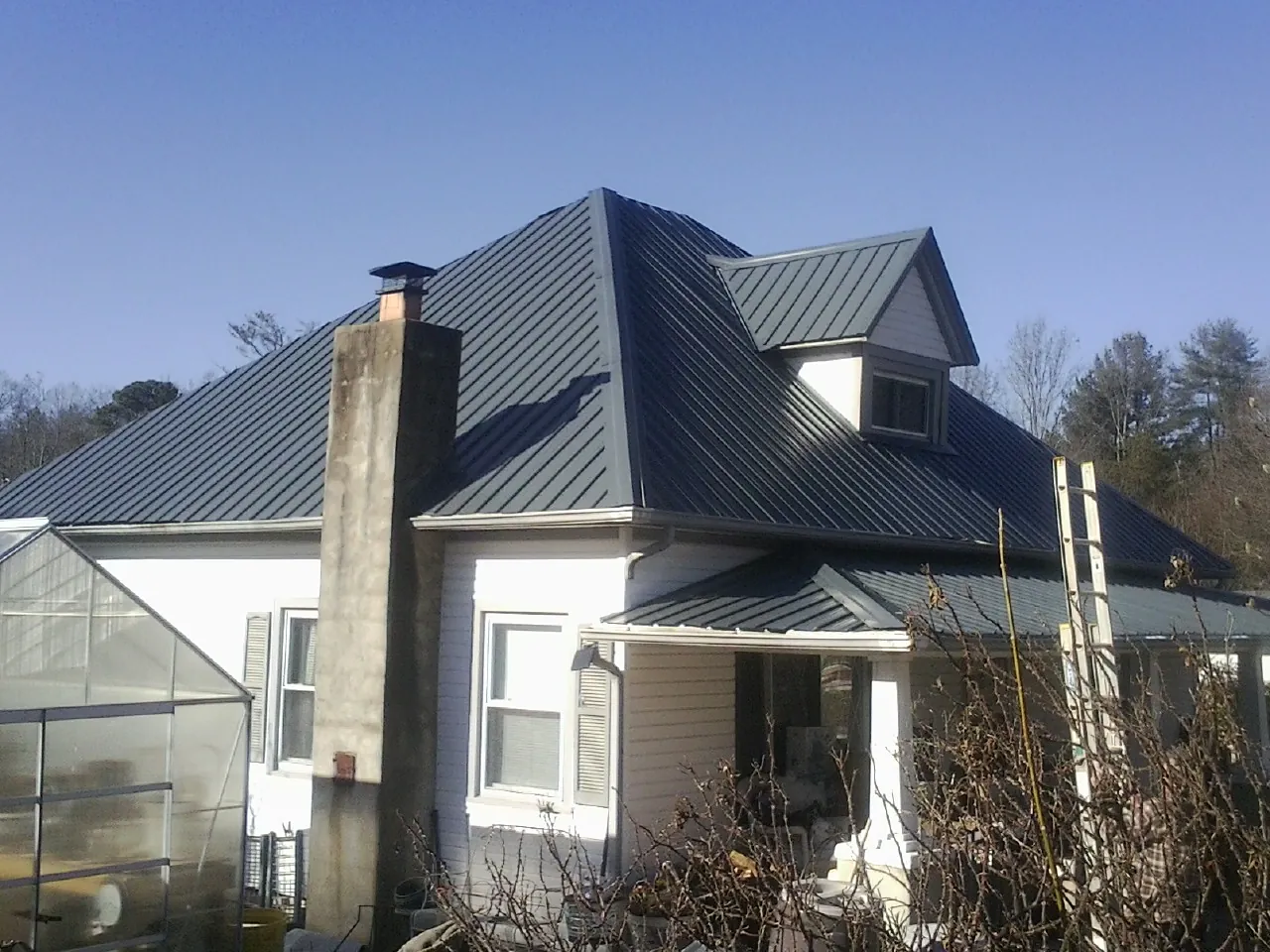 Dark blue standing seam metal roof on a white farmhouse with dormer — Slate & Tile Roof Repair by Roofing Brothers in Sunfield