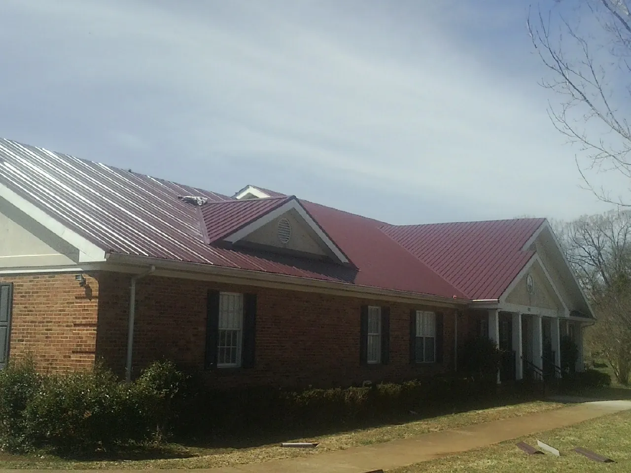 Red metal roof with gabled entries on a long brick building, from a Hail Damage Roof Repair job in Sunfield