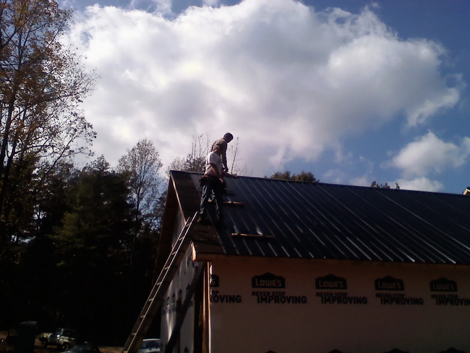 Roofer fastening dark metal panels high against a cloudy sky, from a Roof Inspection job in Sunfield