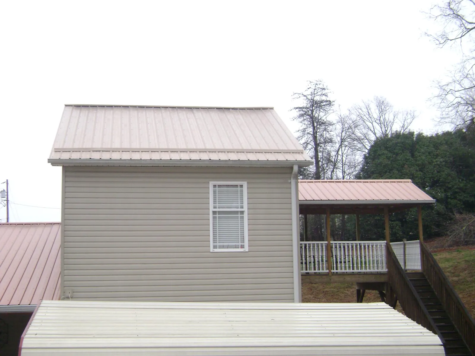 Tan metal roofs on a two story addition and attached porch, from a Roof Replacement job in Sunfield